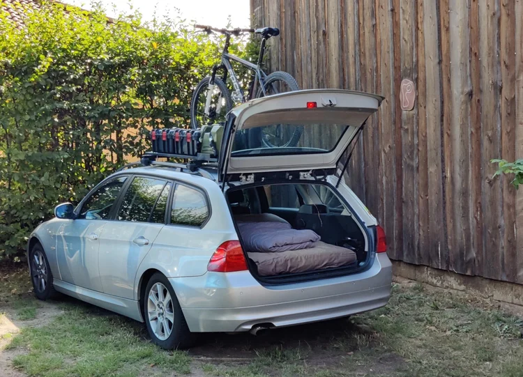 Silberner BMW 3er Touring mit Schlafausbau im Kofferraum und Mountainbike auf dem Dach