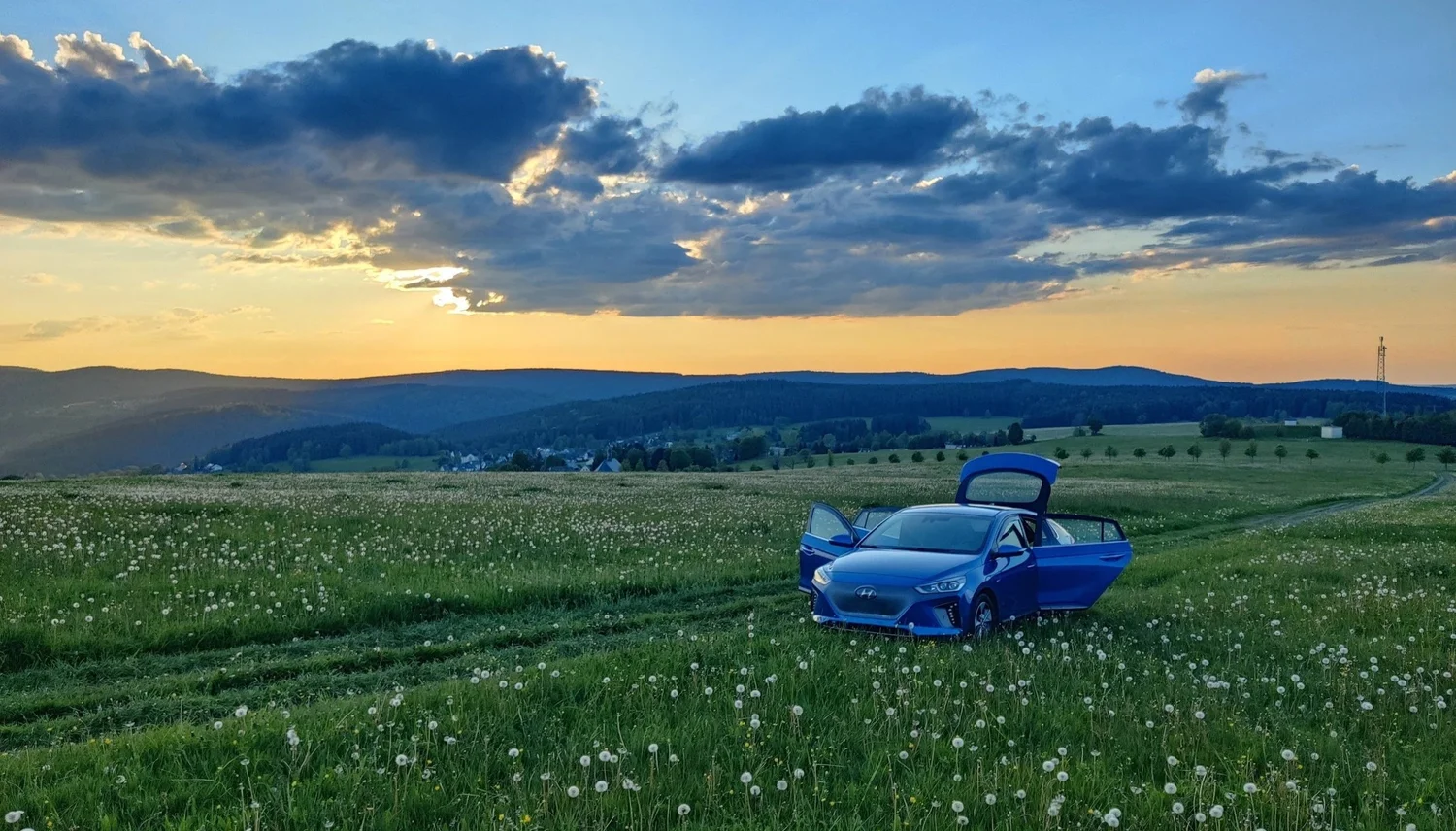 Blauer Hyundai Ioniq mit geöffneten Türen auf einer Blumenwiese bei Sonnenuntergang