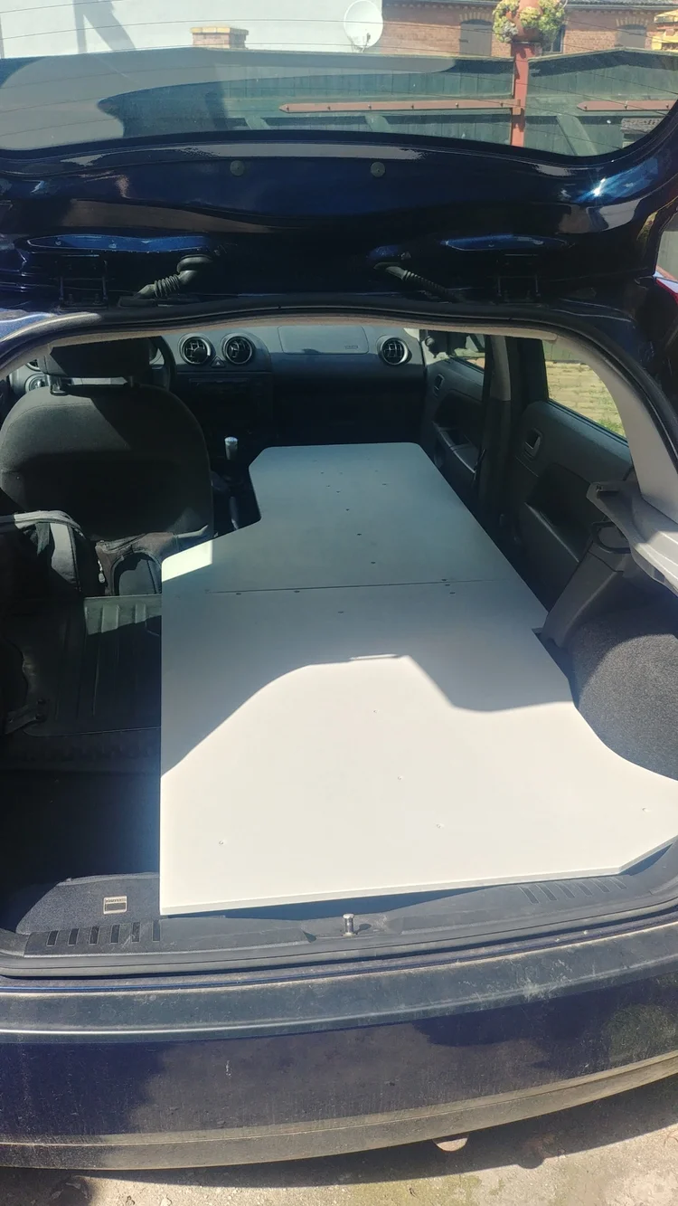 Individueller Camper-Ausbau mit heller, maßgeschneiderter Schlafplatte über den umgeklappten Sitzen eines dunkelblauen Ford Fiesta