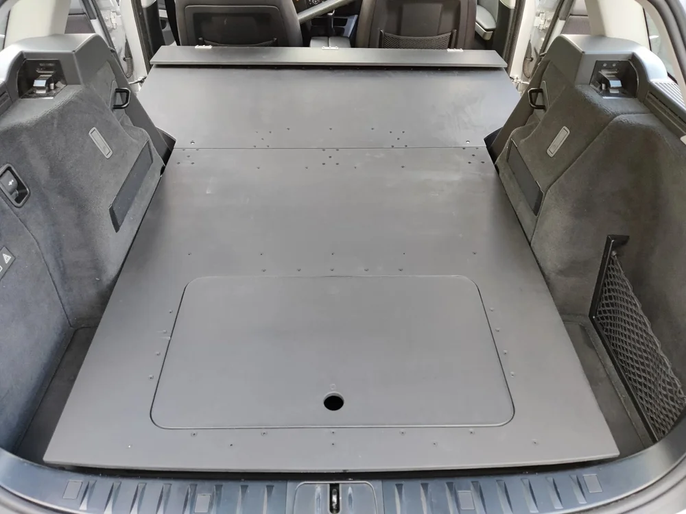 Schwarz beschichtete, ebene Ausbaufläche mit eingelassener Klappe im Kofferraum eines Kombi