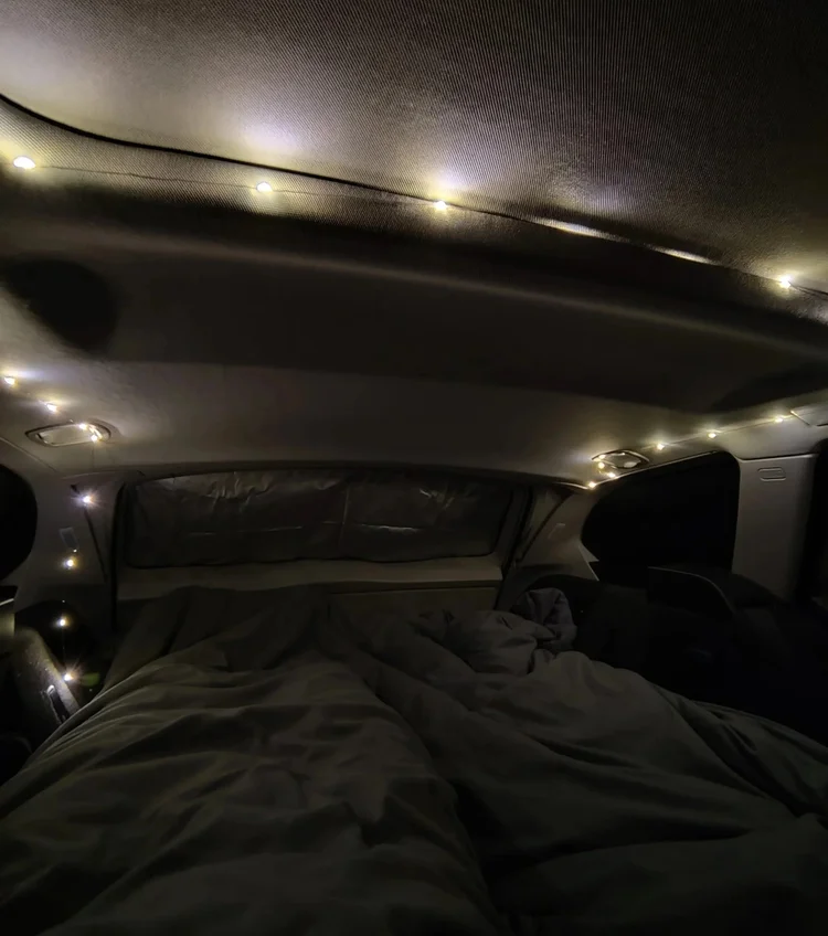 Gemütliches Bett mit Lichterkette bei Nacht im ausgebauten Kombi