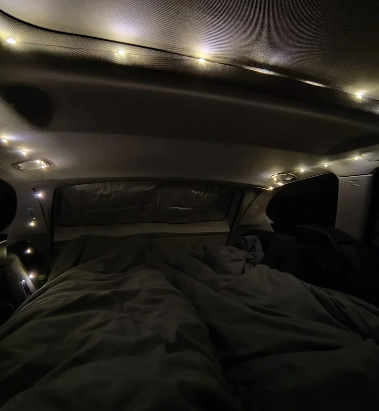 Gemütliches Bett mit Lichterkette bei Nacht im ausgebauten Kombi